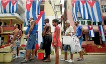  ??  ?? People line up to collect potable water from a government tanker next to Cuban flags hanging out to dry in Cuba’s capital, Havana.