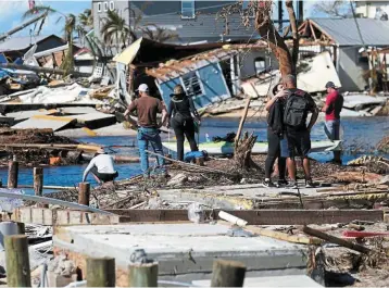  ?? ?? The aftermath: People stand on the destroyed bridge to Pine Island as they view the damage in the aftermath of Hurricane Ian in Florida. The storm is set to be one of the top-10 costliest storms in the US.