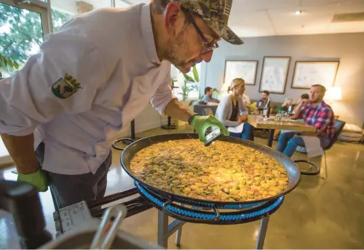  ?? BILL TIERNAN/FREELANCE PHOTOS ?? Daniel Domingo Rodriguez uses his cell phone flashlight to check a pan of paella in Virginia Beach at Tinto Wine & Cheese’s Paella Night on Oct.5.