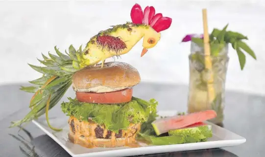  ?? MICHAEL LAUGHLIN/SUN SENTINEL PHOTOS ?? Jonny NoBones parrot topped blackened tiki burger with a triple rum cocktail.
