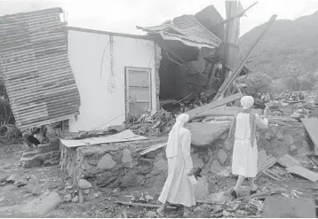  ?? RICKO WAWO/AP ?? Fatal floods, landslides in Indonesia: Nuns walk past a damaged house Tuesday in a flood-affected village on Lembata Island in Indonesia. Multiple disasters caused by torrential rains in eastern Indonesia have killed at least 55 people and displaced thousands, the country’s disaster relief agency said. More than 40 other people were missing.