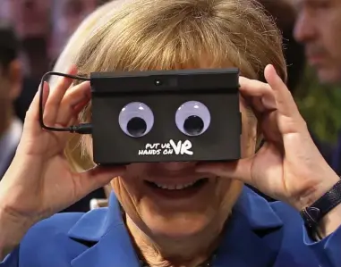 ??  ?? Eye-to-eye: Mrs Merkel tries out the virtual reality camera at a trade fair in Hanover yesterday