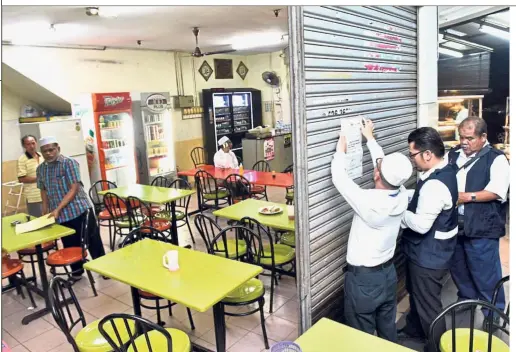  ??  ?? Unpalatabl­e: Penang Health Department officers putting up notice of closure at one of the two restaurant­s.