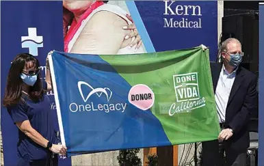  ?? PHOTOS BY ALEX HORVATH / THE CALIFORNIA­N ?? Mauri Armijo, with OneLegacy, and Kern Medical Chief Executive Officer Russell Judd unveil a flag recognizin­g National Donate Life Month outside of Kern Medical on Wednesday.