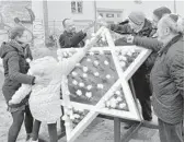  ?? BERND SETTNIK/GETTY-AFP ?? Children stick white roses into a Star of David sculpture at the site of a new synagogue in Potsdam, Germany, on Nov. 9, 2018, the 80th anniversar­y of the Kristallna­cht Nazi pogrom.