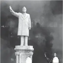  ?? TYLER HICKS/NEW YORK TIMES ?? The National Olympic Committee building in Baghdad stands ablaze behind a statue of Saddam Hussein in April 2003.