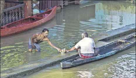  ?? BLOOMBERG ?? A man standing in floodwater shares tea with another man sitting in a canoe in Kerala’s Alappuzha district.