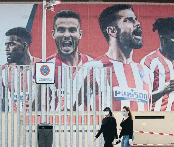  ??  ?? Dos personas transitan ante un mural del Atlético en el estadio Wanda Metropolit­ano de Madrid