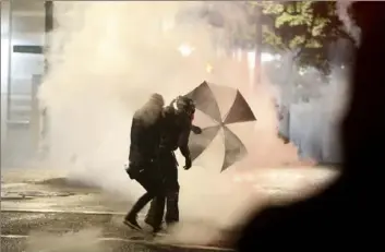  ?? Mark Graves/ The Oregonian via AP ?? Protesters demanding the end of police violence against Black people take cover from smoke during a demonstrat­ion in Portland, Ore., on Wednesday.