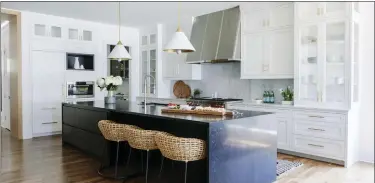  ?? (AIMEE MAZZENGA/FRESH TWIST STUDIO VIA AP) ?? This image released by Fresh Twist Studio shows a kitchen design with woven Palecek kitchen stools and a striking midnight blue stone island to balance the extensive Shaker-style white and glass cabinetry. The brass-toned lining of the pendant fixtures from Circa Lighting is echoed in the cabinet hardware.