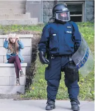  ?? PAUL CHIASSON / THE CANADIAN PRESS ?? A young girl takes a photo on her cellphone beside a police officer in riot gear as he stands watch ahead of a planned G7 protest in Quebec City on Thursday.