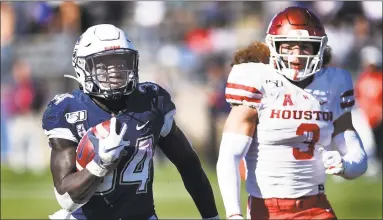  ?? Stephen Dunn / Associated Press ?? UConn running back Kevin Mensah (34) gains yardage against Houston linebacker Jordan Carmouche during the second half on Saturday in East Hartford.