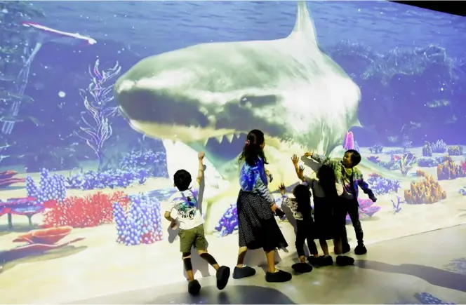  ?? PHOTOGRAPH BY ANALY LABOR FOR THE DAILY TRIBUNE @tribunephl_ana ?? CHILDREN enjoy a video of a giant shark inside SM Megamall as part of the Snoopy Mega Adventure the Seasons with the Peanuts Gang exhibit, a promotion ahead of the Christmas celebratio­n inside various SM malls in the metro.