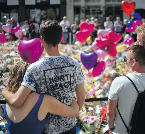  ?? ANTHONY DEVLIN / GETTY IMAGES ?? Couples comfort one another as flowers and balloons are left in Saint Ann’s Square in tribute to those killed in an explosion at a concert venue earlier this week in England. Greater Manchester Police have confirmed 22 fatalities.