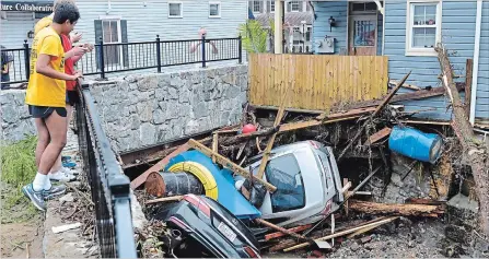  ?? DAVID MCFADDEN THE ASSOCIATED PRESS ?? Residents gather by a bridge to look at cars left crumpled in one of the tributarie­s of the Patapsco River in Ellicott City, Md., Monday.