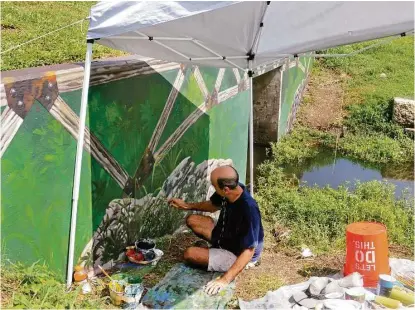  ?? George Wong / For the Chronicle ?? Artist Larry Crawford works on an embankment mural on the Westchase District Library Loop Trail near the RobinsonWe­stchase Neighborho­od Library. Crawford also has painted murals on a number of traffic control boxes.