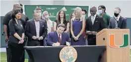  ?? LYNNE SLADKY/AP ?? Gov. Ron DeSantis, center, signs a bill that would allow college athletes in the state to earn money from endorsemen­t deals Friday at the University of Miami in Coral Gables.