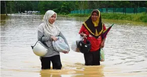  ??  ?? Getting by: Two women braving floodwater­s to buy groceries in Setiu, Terengganu. — Bernama