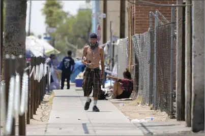  ?? AP photo ?? A pedestrian walks next to a Phoenix homeless encampment as temperatur­es soar past 115 degrees Thursday. Homeless people and those who live in ethnically and racially diverse low-income neighborho­ods are among those especially vulnerable to the heat.