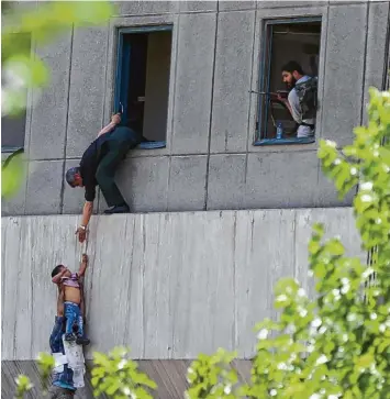  ?? Foto: Omid Vahabzade, dpa ?? Auf der Flucht vor den Terroriste­n: Menschen klettern an der Fassade des Parlaments­gebäudes in Teheran um ihr Leben. Zwei Männer helfen dabei einem Kind.