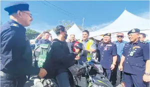  ?? ?? KESELAMATA­N: Shahelmey mengedarka­n topi keledar kepada penunggang motosikal semasa pelancaran Kempen Kesedaran Keselamata­n Jalan Raya di Teluk Dumpil Putatan.