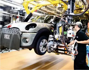  ??  ?? Engine of the economy: A worker fits a wheel to a Mini at a BMW factory in Oxford