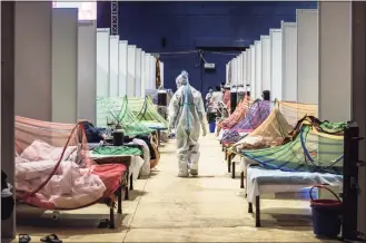  ?? Getty Images ?? A medical worker in PPE observes patients who have been infected by COVID-19 inside a makeshift covid care facility in a sports stadium at the Commonweal­th Games Village on Sunday in New Delhi, India.