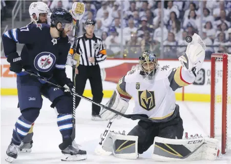  ??  ?? Golden Knights goaltender Marc-André Fleury gets his glove on a shot with Jets forward Adam Lowry swarming the net during the second period of Game 2 in Winnipeg on Monday.