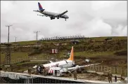  ?? ASSOCIATED PRESS ?? A plane descends to land as soldiers guard the wreckage of a plane operated by Pegasus Airlines after it skidded off the runway Wednesday at Istanbul’s Sabiha Gokcen Airport, killing three and injuring dozens.