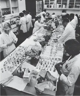  ?? CHARLIE KNOBLOCK/AP ?? Workers test Tylenol medication for the presence of cyanide at a Chicago City Health Department lab. In that era, many people did not wear gloves while handling evidence or conducting tests.