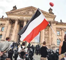  ?? FOTO: SOMMER/DPA ?? Teilnehmer einer Kundgebung gegen die Corona-Maßnahmen stehen im August 2020 vor dem Reichstag in Berlin, ein Teilnehmer hält eine Reichsfahn­e. Jetzt wollen die Innenminis­ter geschlosse­n gegen den Missbrauch der Fahnen vorgehen.