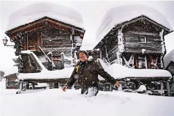  ?? FOTO: DPA ?? Ein Mann geht in Bellwald in der Schweiz an schneebede­ckten Hütten vorbei. In den vergangene­n Tagen hat es in Teilen der Schweiz und in Österreich massiv geschneit.