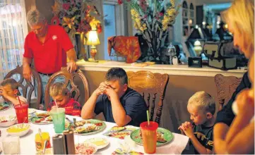  ?? PHOTOS BY SARAH PHIPPS, THE OKLAHOMAN ?? Below: The Mathes family prays before dinner at their home. From left are Bryce, Stephen, Brent, Blake, Nathan, Cathy and Kyleigh.