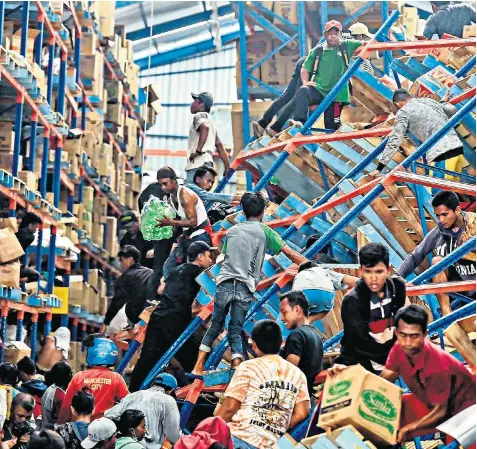  ??  ?? Survivors in Palu clamber over collapsed shelving as they desperatel­y search a damaged warehouse for supplies. Food and medical supplies are running critically short