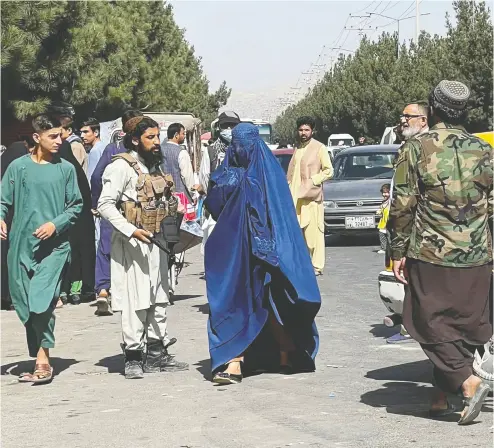  ?? STRINGER / REUTERS ?? Taliban forces block the roads around the Kabul airport, while a woman passes by on Friday. After Canada announced its last flight out of Afghanista­n, many cooks, guards and translator­s were left stranded.