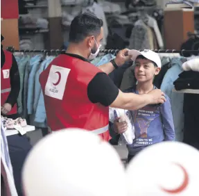  ??  ?? A Turkish Red Crescent worker gives new clothes to a Syrian boy, in Azaz, Syria, July 18, 2021.