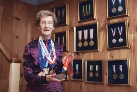  ?? CRESTINA MARTINS GRAND MAGAZINE ?? Jean Horne holds and wears medals won as a race walker. On the wall are medals from her running days.