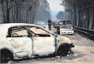  ??  ?? A policeman walks on a road past burnt cars in Figueiro dos Vinhos