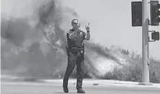  ??  ?? A police officer turns traffic away as flames leap behind him in Carlsbad, California. ASSOCIATED PRESS