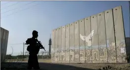  ?? ASSOCIATED PRESS FILE PHOTO ?? A member of Israeli forces stands next to a security wall with Hebrew writing reading “Path to Peace” at the Kibbutz Netiv Haasara near the border with Gaza Strip, Israel, on November 17, 2023.