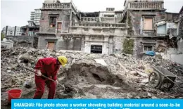  ??  ?? SHANGHAI: File photo shows a worker shoveling building material around a soon-to-be torn down and empty residentia­l building in Shanghai. —AFP