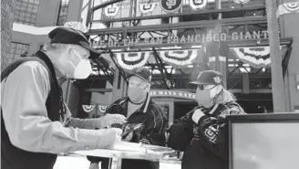  ?? DAI SUGANO/TRIBUNE NEWS SERVICE ?? San Francisco Giants fans Dave Harding, center, and his wife, Nancy Faltisek, check in at one of the vaccinatio­n verificati­on booths before being admitted to Oracle Park at the Giants’ home opener on April 9 in San Francisco.