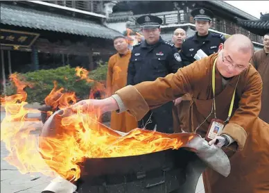  ?? FAN JUN / XINHUA ?? A monk attempts to put out a fire using a blanket during a fire-control training session at Zhenru Monastery in Shanghai on Wednesday. A firefighti­ng squad comprised of 12 monks was recently establishe­d at the temple, which has a nearly 80-year...