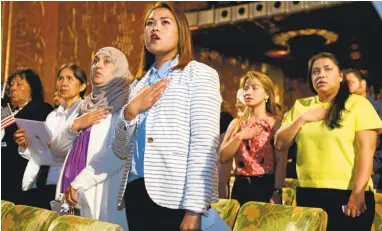  ?? ANDA CHU/STAFF PHOTOS ?? Citizenshi­p applicants stand during the singing of the national anthem at a naturaliza­tion ceremony at the Paramount Theatre.