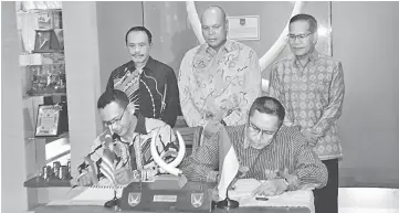  ??  ?? Stephen (standing centre), Widodo (standing right) and Bustaman (standing left) witness the signing of the MoU by Wan Edenin (seated left) and Denny. — Photo by Wilfred Pilo