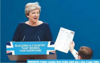  ?? —AFP ?? MANCHESTER: Protester comedian Simon Brodkin (right) gives a piece of paper written as a mock P45 (employee leaving form) to Britain’s Prime Minister Theresa May as she was delivering her speech on the final day of the Conservati­ve Party annual...