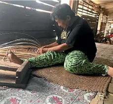  ??  ?? A woman weaves a floor mat using dried palm leaves.