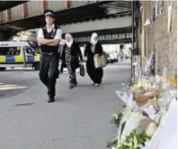  ??  ?? A police officer and members of the public walk past flowers, close to Finsbury Park Mosque