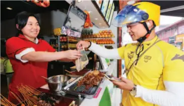  ??  ?? June 13, 2016, Xiangyang City, Hubei Province: Yang Jingbing, a Meituan Waimai delivery driver, picks up food for the customer. As a gym coach, Yang likes his part-time job as a delivery driver because of its flexible schedule. VCG