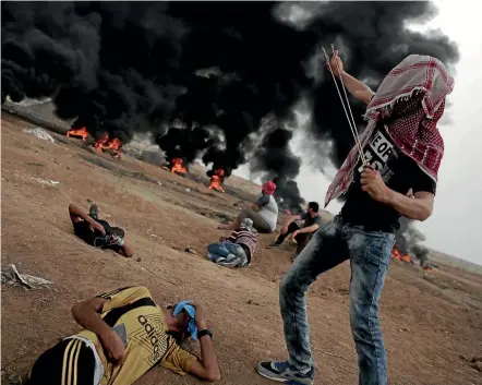  ?? PHOTO: AP ?? A Palestinia­n protester fires stones at Israeli troops as others are incapacita­ted by tear gas during yesterday’s protest at the Gaza Strip’s border with Israel.